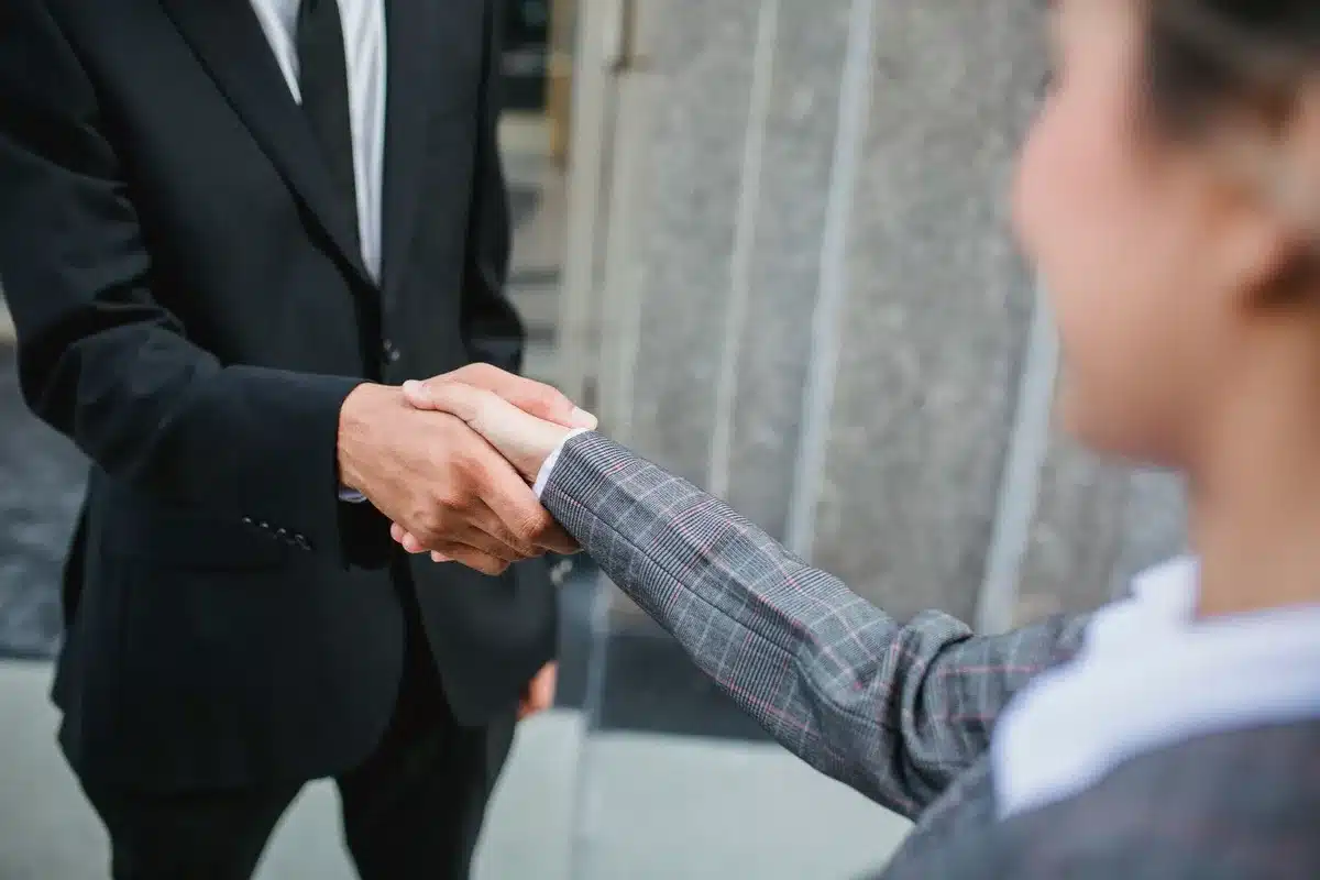 Stretta di mano tra due figure anonime su sfondo di edifici bancari e grafici finanziari