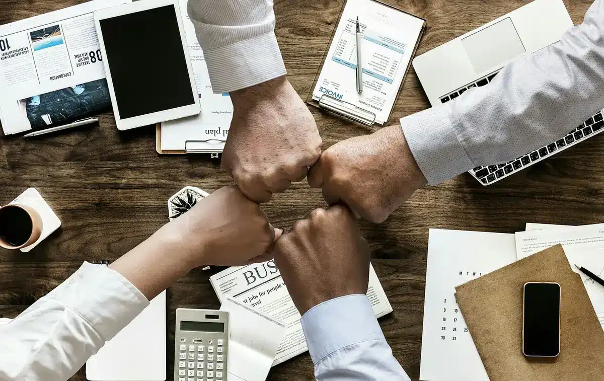 Mani che tengono smartphone con grafici finanziari sfocati su scrivania domestica