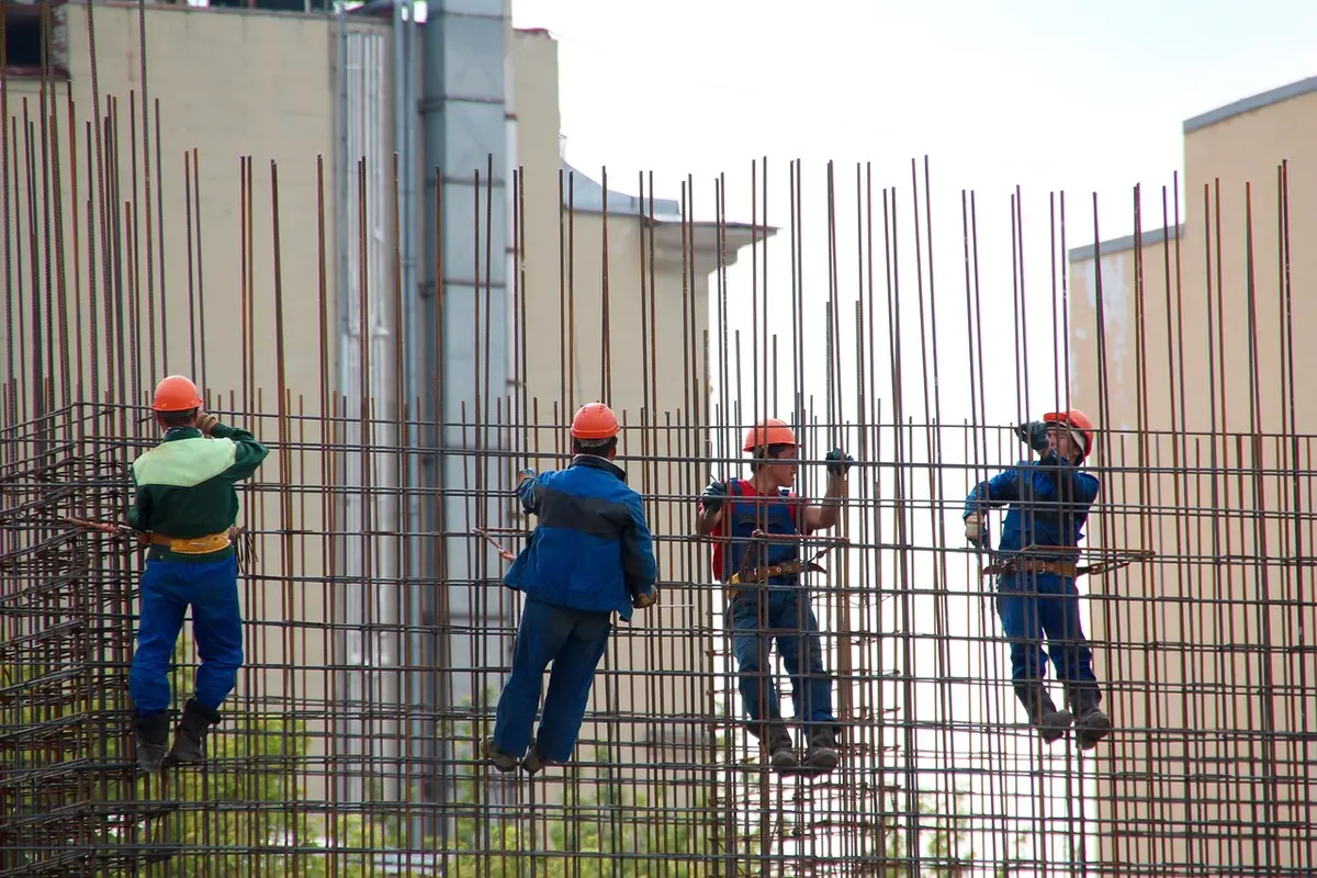 Operai anonimi e planimetrie su un tavolo di cantiere con impalcature sullo sfondo
